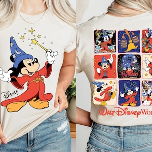 May include: Cream-colored t-shirt featuring a graphic of Mickey Mouse as a sorcerer, holding a wand with stars. The back of the shirt displays Mickey in various poses, with "Walt Disney World" text. The shirt is made of soft cream-colored material.