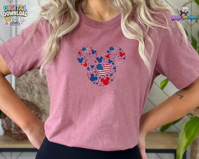 Puede incluir: Una camiseta de manga corta color malva con un gr&aacute;fico central de una gran silueta de cabeza de Mickey Mouse compuesta por iconos m&aacute;s peque&ntilde;os de cabezas de Mickey, estrellas y patrones de bandera estadounidense en rojo, blanco y azul.
