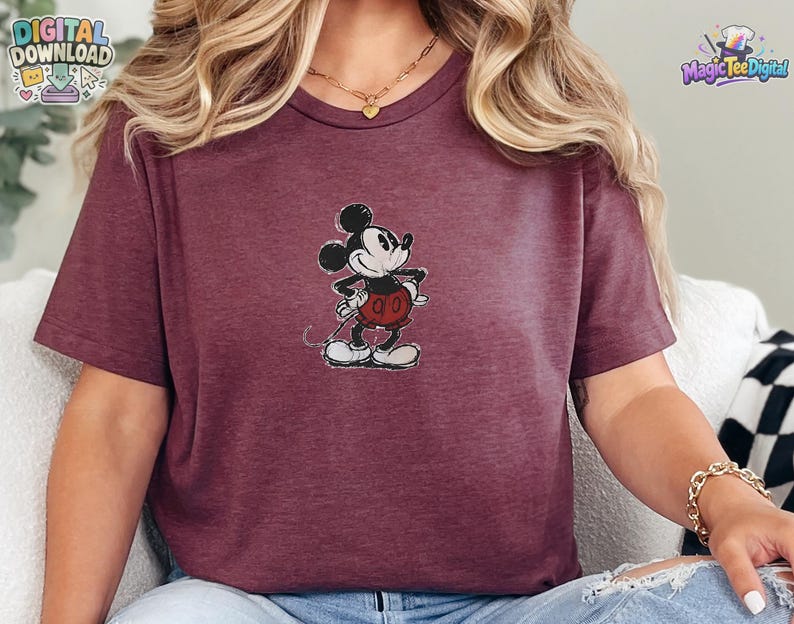 May include: A maroon short-sleeved t-shirt featuring a centered graphic of a vintage-style Mickey Mouse character. The character is depicted in black, white, and red with a distressed texture. The shirt has a crew neckline and a heathered fabric finish.