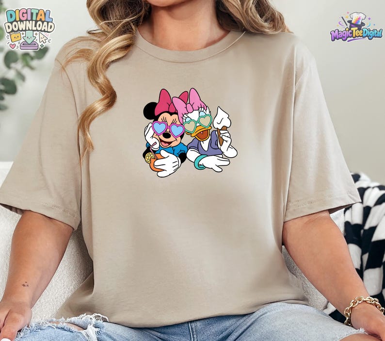 May include: A beige short-sleeved t-shirt featuring a graphic print of Minnie Mouse and Daisy Duck wearing heart-shaped sunglasses. Minnie holds an orange drink with a straw, while Daisy holds a white ice cream cone. The design is centered.