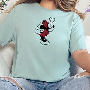 May include: A light mint green short-sleeved t-shirt featuring a black and red graphic of a cartoon mouse character blowing a kiss with a small black heart outline above the character's head. The shirt has a crew neckline and a standard fit.