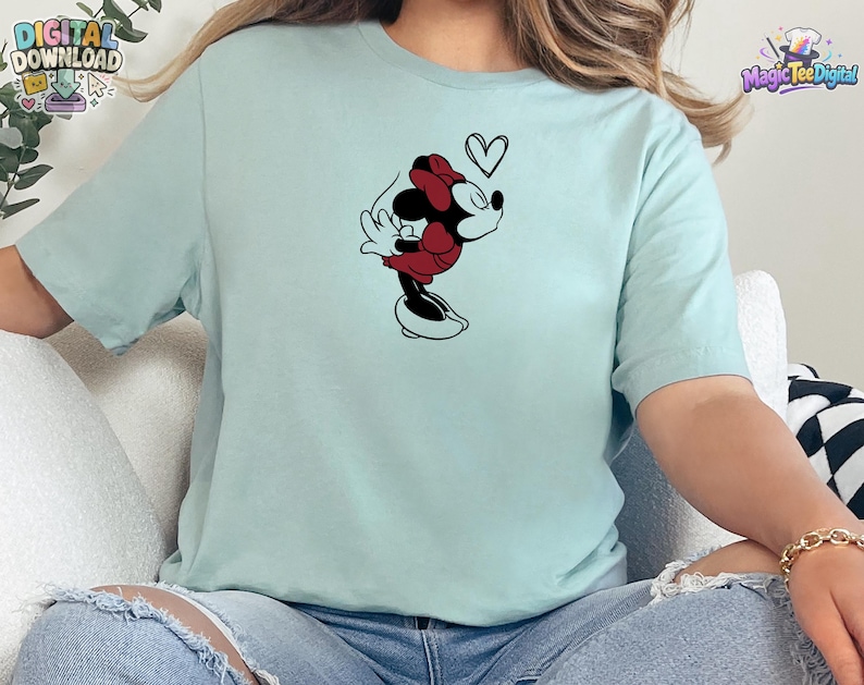 May include: A light mint green short-sleeved t-shirt featuring a black and red graphic of a cartoon mouse character blowing a kiss with a small black heart outline above the character's head. The shirt has a crew neckline and a standard fit.