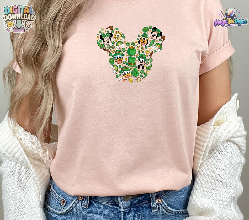 Pu&ograve; includere: Una t-shirt a maniche corte color rosa chiaro con una grafica centrale a forma di silhouette di testa di topo. Il disegno &egrave; composto da vari personaggi dei cartoni animati con cappelli verdi, trifogli, monete d'oro e pentole d'oro.