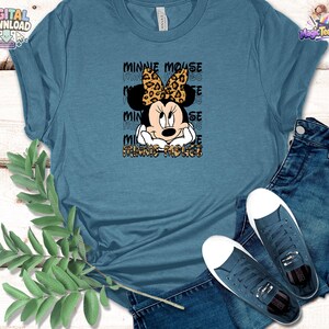 Pode incluir: Uma t-shirt azul ard&oacute;sia com um gr&aacute;fico da Minnie Mouse com um la&ccedil;o de padr&atilde;o leopardo. O texto MINNIE MOUSE &eacute; repetido no fundo com um tipo de letra de contorno preto e o nome aparece novamente na parte inferior com padr&atilde;o leopardo.