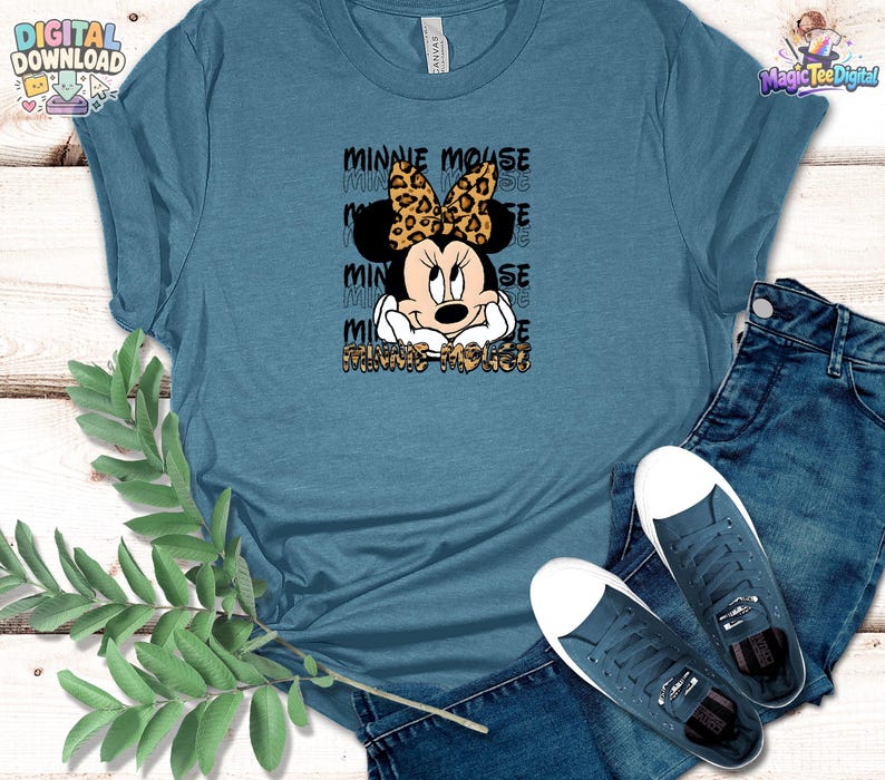Pode incluir: Uma t-shirt azul ard&oacute;sia com um gr&aacute;fico da Minnie Mouse com um la&ccedil;o de padr&atilde;o leopardo. O texto MINNIE MOUSE &eacute; repetido no fundo com um tipo de letra de contorno preto e o nome aparece novamente na parte inferior com padr&atilde;o leopardo.