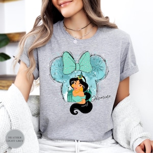 Puede incluir: Camiseta gris jaspeado claro con una ilustraci&oacute;n de dibujos animados de la Princesa Jasmine dentro de un dise&ntilde;o en forma de Mickey Mouse. El dise&ntilde;o incluye un lazo turquesa, un castillo y el nombre "Jasmine".