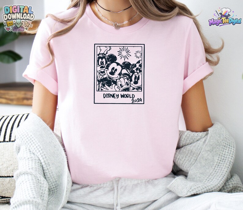 K&ouml;nnte beinhalten: Ein hellrosa T-Shirt mit einem schwarzen Grafikdruck eines quadratischen Rahmens im Polaroid-Stil, der Zeichentrickfiguren wie Mickey Maus, Minnie Maus, Donald Duck und Goofy enth&auml;lt, mit dem Text Disney World 2024 unter dem Rahmen.