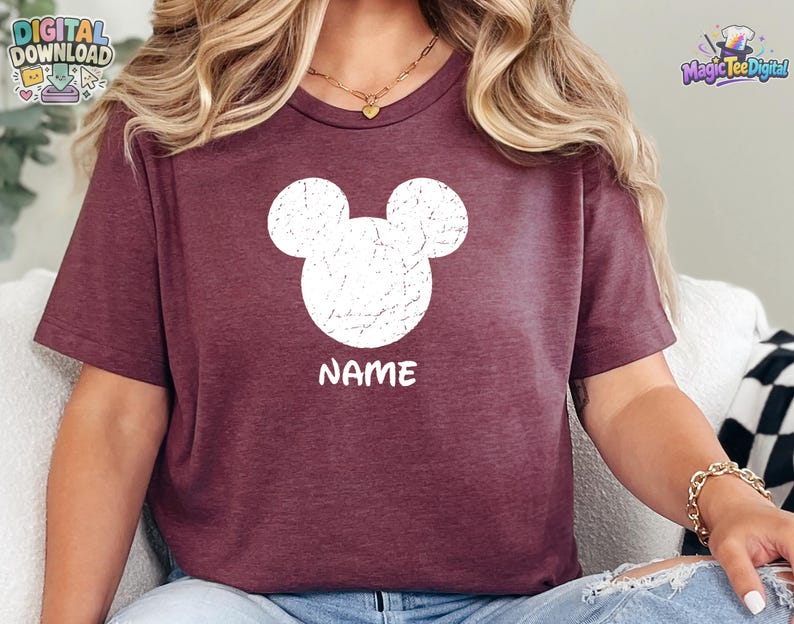 May include: A maroon short-sleeved t-shirt featuring a white distressed graphic of a mouse head silhouette centered on the chest. Below the mouse head graphic, the word NAME is printed in a bold, white, sans-serif font on the front of the shirt.