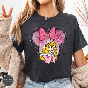May include: Dark grey t-shirt with a Minnie Mouse-shaped design, a pink bow, and a princess illustration. The design includes the name "Aurora". A comfortable, casual wear t-shirt.