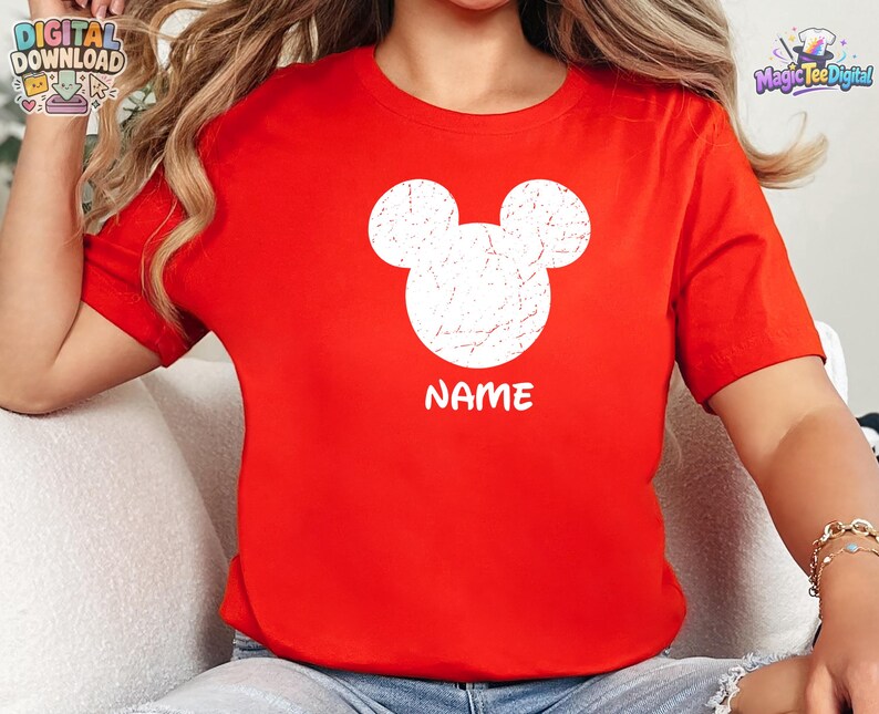 May include: A bright red short-sleeved t-shirt featuring a large, white, distressed-texture Mickey Mouse head silhouette centered on the chest. Below the graphic, the word NAME is printed in a bold, white, sans-serif font.