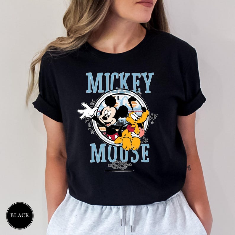 May include: Black t-shirt featuring a graphic of Mickey Mouse and Pluto. The design includes the words "Mickey Mouse" in blue, with Mickey Mouse waving and Pluto sitting. The shirt is a classic crew neck.