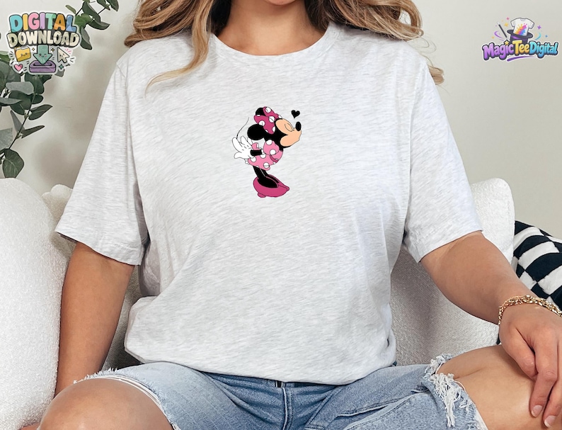 May include: A light gray heathered short-sleeve t-shirt featuring a centered graphic of a cartoon mouse character wearing a pink polka-dot dress and bow, blowing a kiss with a small black heart icon floating near the character's face.