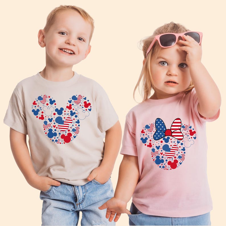 May include: Two children wearing matching t-shirts. The shirts feature a Mickey Mouse head design filled with red, white, and blue shapes and patterns. One shirt is tan, the other is pink. The design includes stars, stripes, and Mickey Mouse silhouettes.