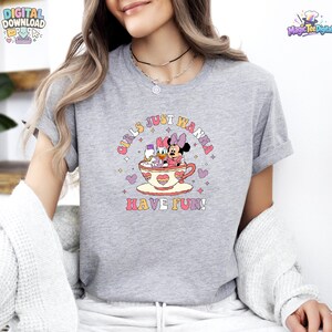 May include: A heather gray t-shirt featuring a graphic of Minnie Mouse and Daisy Duck sitting inside a large teacup. The text "GIRLS JUST WANNA HAVE FUN!" is printed in a curved, colorful font above and below the teacup illustration.