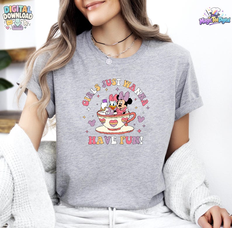 May include: A heather gray t-shirt featuring a graphic of Minnie Mouse and Daisy Duck sitting inside a large teacup. The text "GIRLS JUST WANNA HAVE FUN!" is printed in a curved, colorful font above and below the teacup illustration.