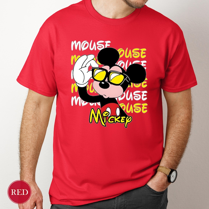 May include: Red t-shirt featuring a cartoon Mickey Mouse character wearing yellow sunglasses. The design includes the word "MOUSE" repeated in a stacked pattern, with "Mickey" in yellow script. The shirt is short-sleeved.