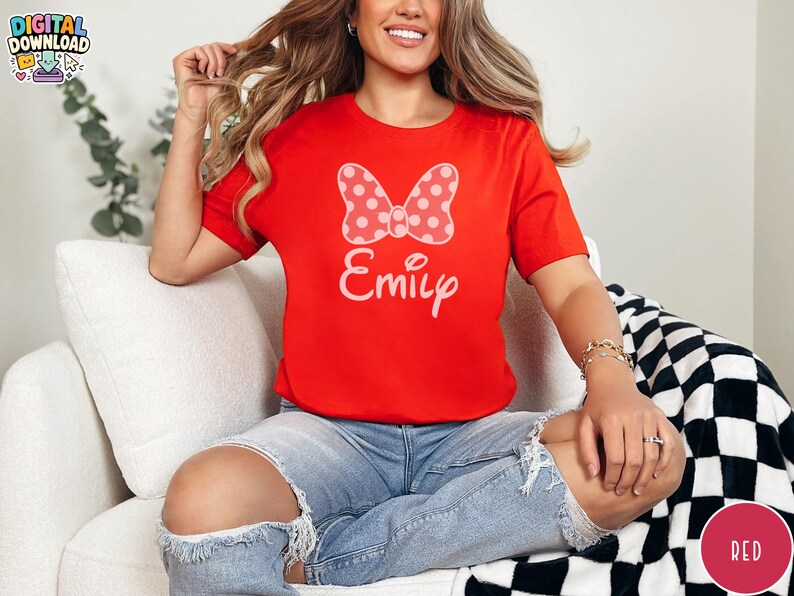May include: A red t-shirt featuring a white polka-dot bow and the name "Emily" in a script font. The shirt is a crew neck style and is made of a soft material. The shirt is a digital download.