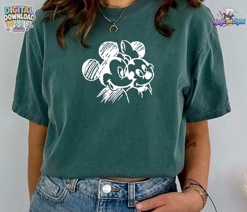May include: A dark green short-sleeved t-shirt featuring a white graphic print of two cartoon mouse characters on the chest. The design is rendered in a sketch-like style with visible line work. The shirt is paired with blue denim jeans.