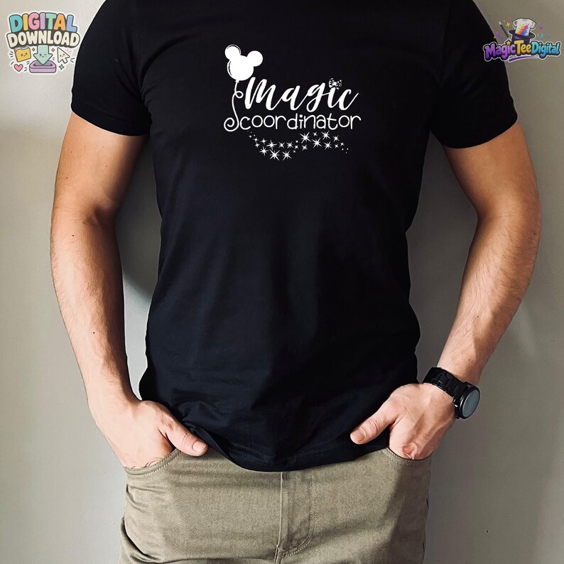 May include: A black short-sleeved t-shirt featuring a white graphic print on the chest. The design includes a balloon shaped like a mouse head, the text "magic coordinator" in a cursive font, and a trail of small sparkling star icons below.