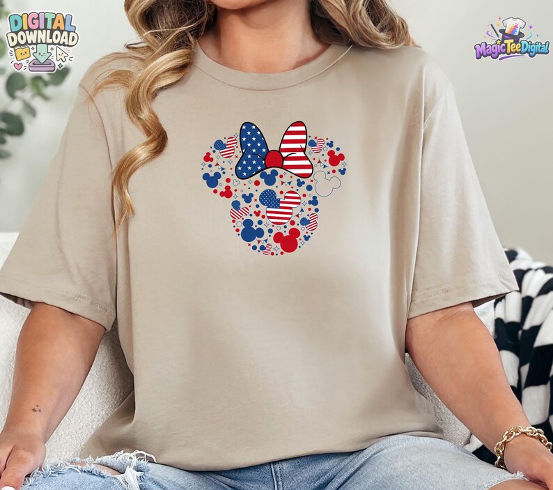 Puede incluir: Una camiseta beige de manga corta con un gr&aacute;fico central de una silueta de cabeza de rat&oacute;n compuesta por iconos m&aacute;s peque&ntilde;os en rojo, blanco y azul, incluyendo patrones de estrellas y rayas, rematada con un gran lazo de dise&ntilde;o patri&oacute;tico.