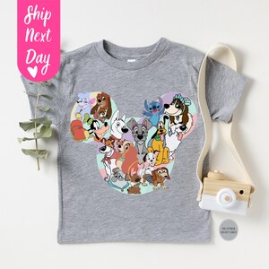 May include: A heather gray t-shirt featuring a colorful graphic of various cartoon dogs arranged in a Mickey Mouse head shape. The shirt has short sleeves and a crew neck. The text "Ship Next Day" is on a pink tag.