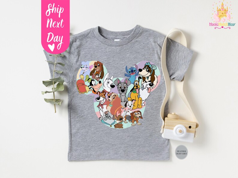 May include: A heather gray t-shirt featuring a colorful graphic of various cartoon dogs arranged in a Mickey Mouse head shape. The shirt has short sleeves and a crew neck. The text "Ship Next Day" is on a pink tag.