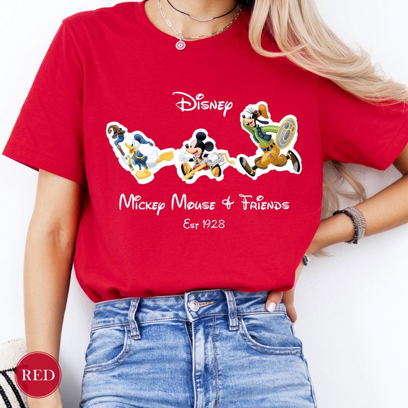 May include: Red t-shirt featuring Disney characters Mickey Mouse, Donald Duck, and Goofy. The shirt has the Disney logo and the text "Mickey Mouse & Friends Est 1928" in white. The shirt is made of a soft material.