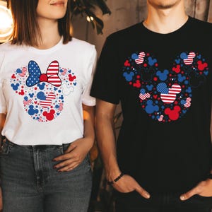 May include: White and black t-shirts featuring a patriotic Mickey Mouse design. The design incorporates red, white, and blue elements, including stars, stripes, and Mickey Mouse silhouettes, creating a festive and themed look.