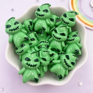 Puede incluir: Una colección de pequeños dijes con forma de fantasma de color verde claro con acabados brillantes. Cada dije presenta una boca cosida en negro pintada a mano y cuencas oculares oscuras y huecas, imitando un diseño de personaje.