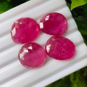 Puede incluir: Cuatro piedras preciosas de color rosa vibrante, con forma ovalada y talladas en facetas, dispuestas en grupo. Cada piedra presenta una superficie pulida con facetas geométricas que reflejan la luz, mostrando un tono magenta intenso.