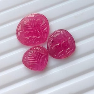 May include: Three vibrant fuchsia-coloured gemstones, each carved with a delicate leaf-like pattern. The stones are rounded and polished, displaying a translucent quality with deep pink hues and intricate, etched lines forming a central vein.