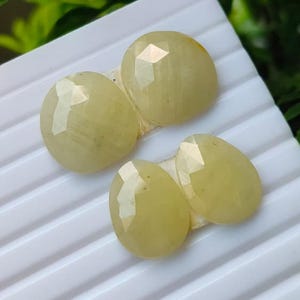 May include: Four faceted, pale yellow, oval-shaped gemstones arranged in a cluster. Each stone features a polished, multi-faceted surface that reflects light, showcasing a translucent, light chartreuse hue and a smooth, rounded edge profile.