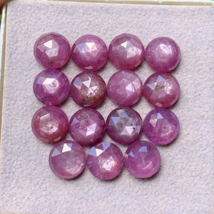 May include: A collection of fourteen round, faceted pink gemstones arranged in a grid pattern. Each stone features a rose-colored hue with a polished, multi-faceted surface that reflects light, creating a sparkling appearance across the stones.