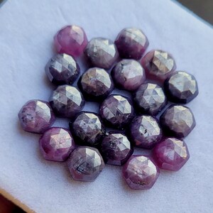 Puede incluir: Un conjunto de gemas facetadas y redondas en tonos morados y rosas. Las gemas tienen una superficie pulida y reflectante, y están dispuestas juntas. La imagen muestra la belleza natural de las piedras, adecuadas para la fabricación de joyas.