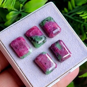 May include: Four rectangular faceted gemstones featuring a mix of vibrant magenta-pink and deep forest green mineral inclusions. The stones are arranged in a display box with a light grey felt lining, showcasing their polished surfaces and edges.