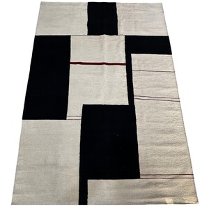 Full view of geometric kilim rug with Bauhaus inspired black and cream pattern displayed on marble floor