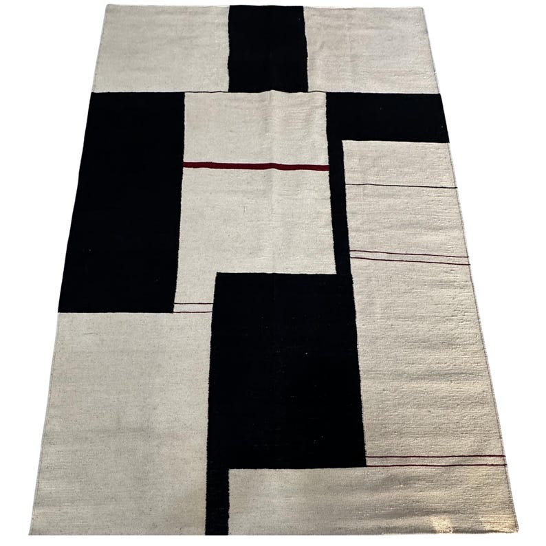 Full view of geometric kilim rug with Bauhaus inspired black and cream pattern displayed on marble floor