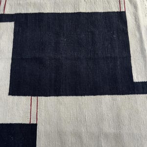 Detailed close-up of handmade wool kilim rug featuring abstract geometric pattern in cream, black and subtle red accents