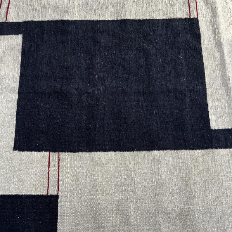 Detailed close-up of handmade wool kilim rug featuring abstract geometric pattern in cream, black and subtle red accents