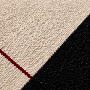 Close-up of a handmade geometric wool rug showing ivory and black sections with a thin red accent line, highlighting the dense handwoven texture and premium craftsmanship.