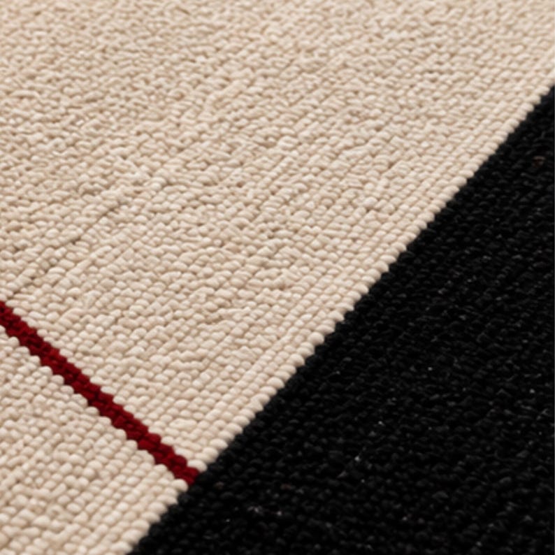 Close-up of a handmade geometric wool rug showing ivory and black sections with a thin red accent line, highlighting the dense handwoven texture and premium craftsmanship.