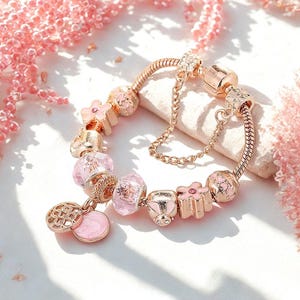 Peut inclure: Un bracelet de charme en or rose avec divers charms roses et dorés. Les breloques comprennent des formes de fleurs, des perles roses transparentes et un charm rond avec un motif décoratif. Une chaîne de sécurité est incluse.