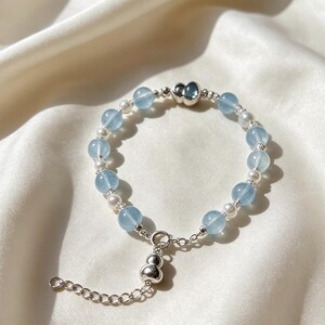 Puede incluir: Una pulsera de cuentas que alterna cuentas redondas translúcidas de color azul claro y pequeñas perlas blancas, acentuada con espaciadores plateados y un dije plateado en forma de calabaza, con cadena extensora y cierre plateados.