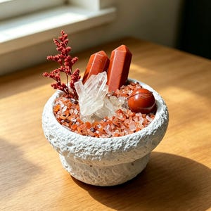 Peut inclure: Un bol blanc texturé rempli de petits éclats de pierre orange et rouge, deux pointes de cristal de jaspe rouge, un amas de quartz clair, une petite sphère de jaspe rouge et un brin de fleurs de statice rouge séchées en décoration.
