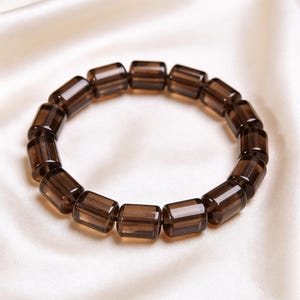 Puede incluir: Una pulsera compuesta por cuentas cilíndricas de color marrón oscuro translúcido. Las cuentas están dispuestas en un patrón circular, cada una con una superficie lisa y pulida que refleja la luz, creando una apariencia consistente en toda la pieza.