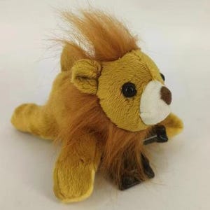 May include: A plush lion toy with a golden-yellow body and a brown mane. The lion has black eyes, a white muzzle, and a brown nose. The toy is lying down, with its paws extended. The lion's mane is made of soft, fluffy material.