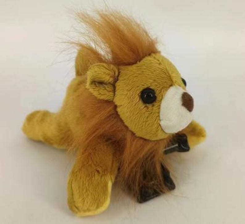 May include: A plush lion toy with a golden-yellow body and a brown mane. The lion has black eyes, a white muzzle, and a brown nose. The toy is lying down, with its paws extended. The lion's mane is made of soft, fluffy material.