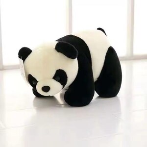May include: A plush panda bear toy in a playful pose. The panda has a black and white color scheme, with black ears, eye patches, and limbs. The soft toy is made of a fluffy material and is positioned on a white surface.