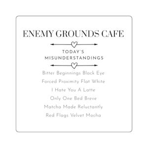 May include: A square white sign with black text reading ENEMY GROUNDS CAFE, TODAY'S MISUNDERSTANDINGS, and a list of coffee-themed items including Bitter Beginnings Black Eye, Forced Proximity Flat White, I Hate You A Latte, Only One Bed Breve, Matcha Made Reluctantly, and Red Flags Velvet Mocha.