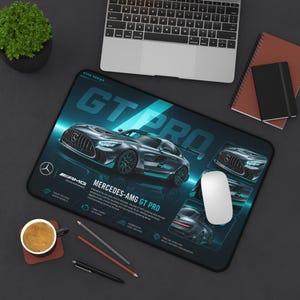 May include: Black rectangular mousepad featuring a Mercedes-AMG GT Pro car design. The mousepad has a dark background with teal accents and the text "GT PRO". Additional text includes "AMG" and car specifications. A white mouse is on the pad.